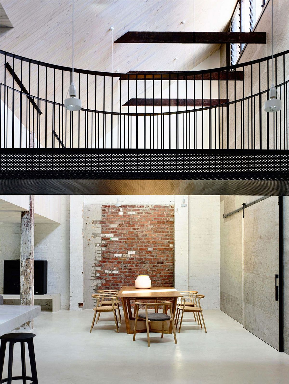 Dining room with exposed brick wall backdrop and a metallic bridge above