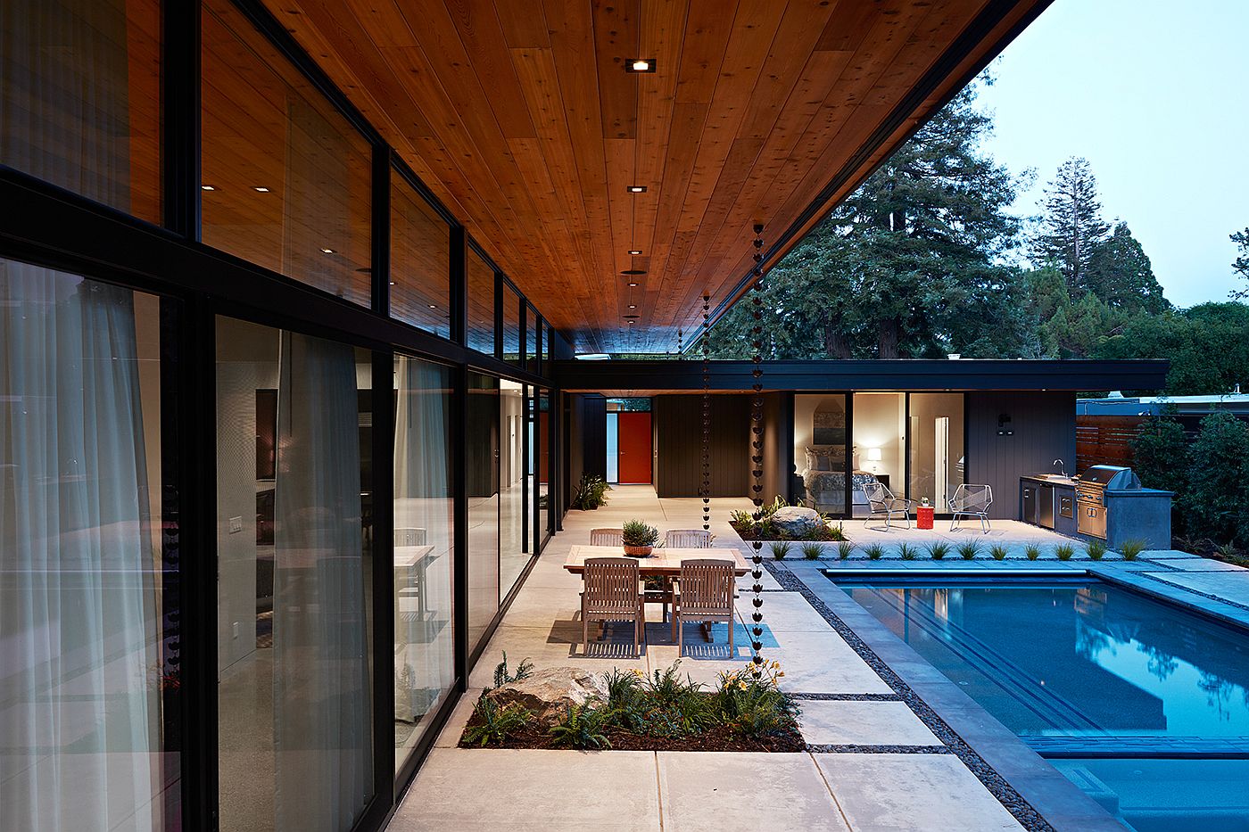 Sliding glass doors and glass walls connect the living area with the landscape and pool outside