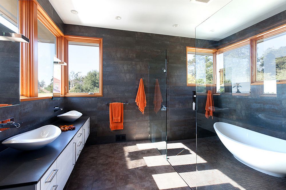 Window frames and towels in orange add a cool, colorful touch to the serene bathroom in gray