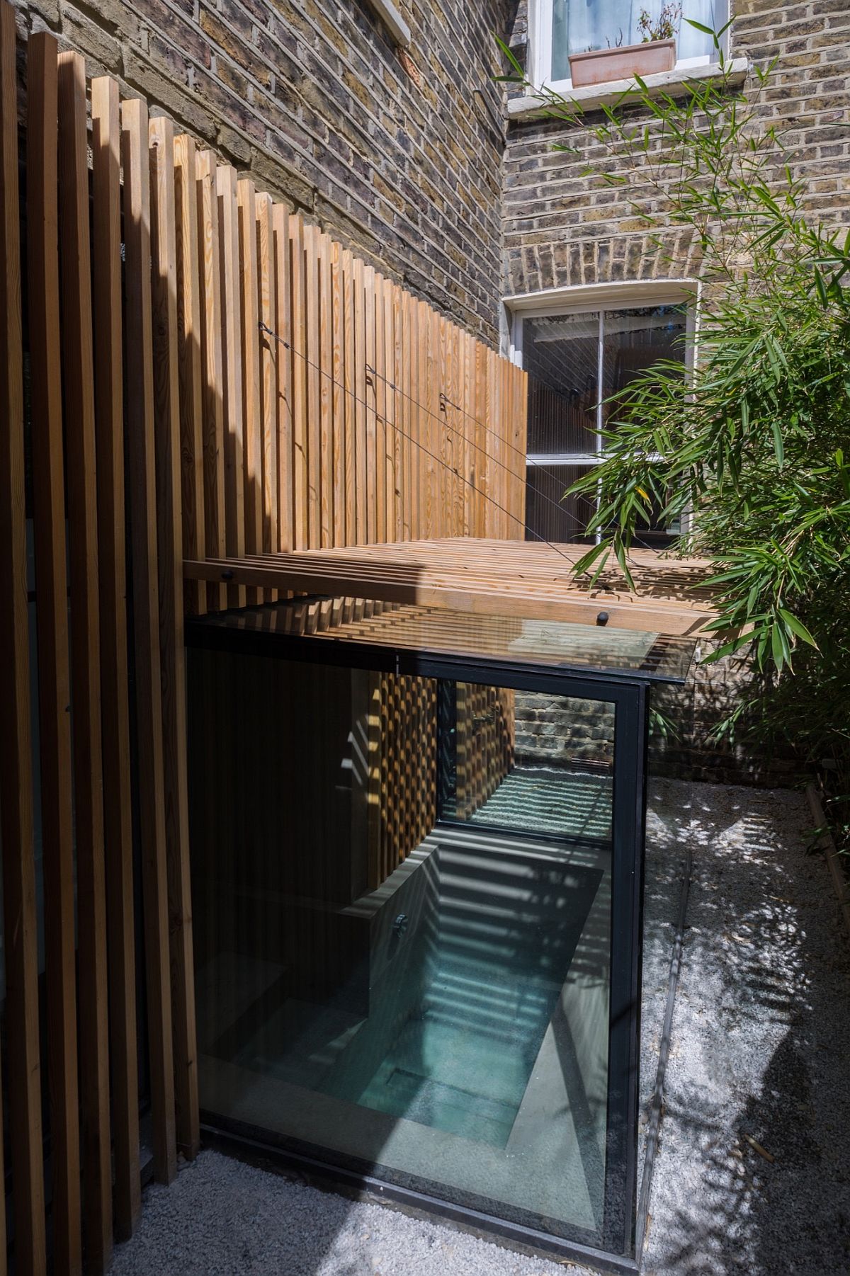 Glass walls connect teh sunken bath with the garden even as the slatted larch screen offers privacy