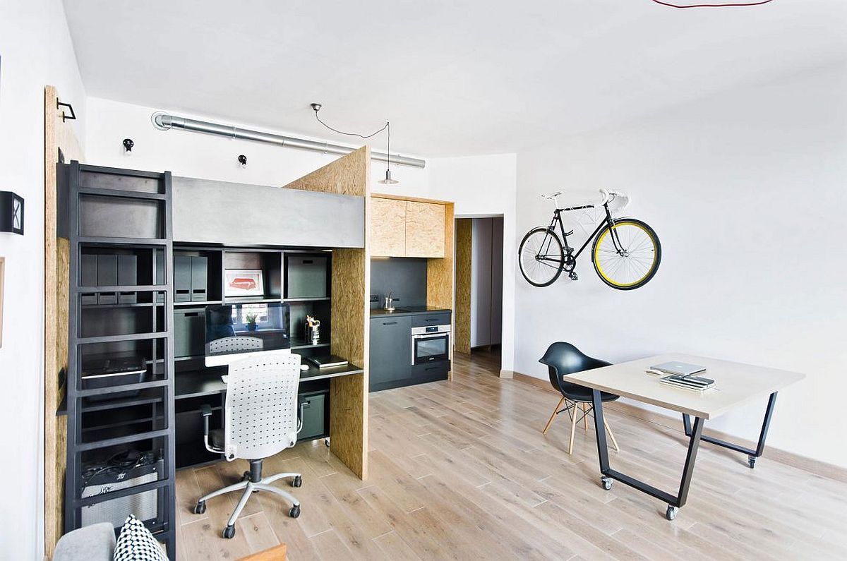 Studio apartment with plywood room dividers and work desk under an elevated bed.