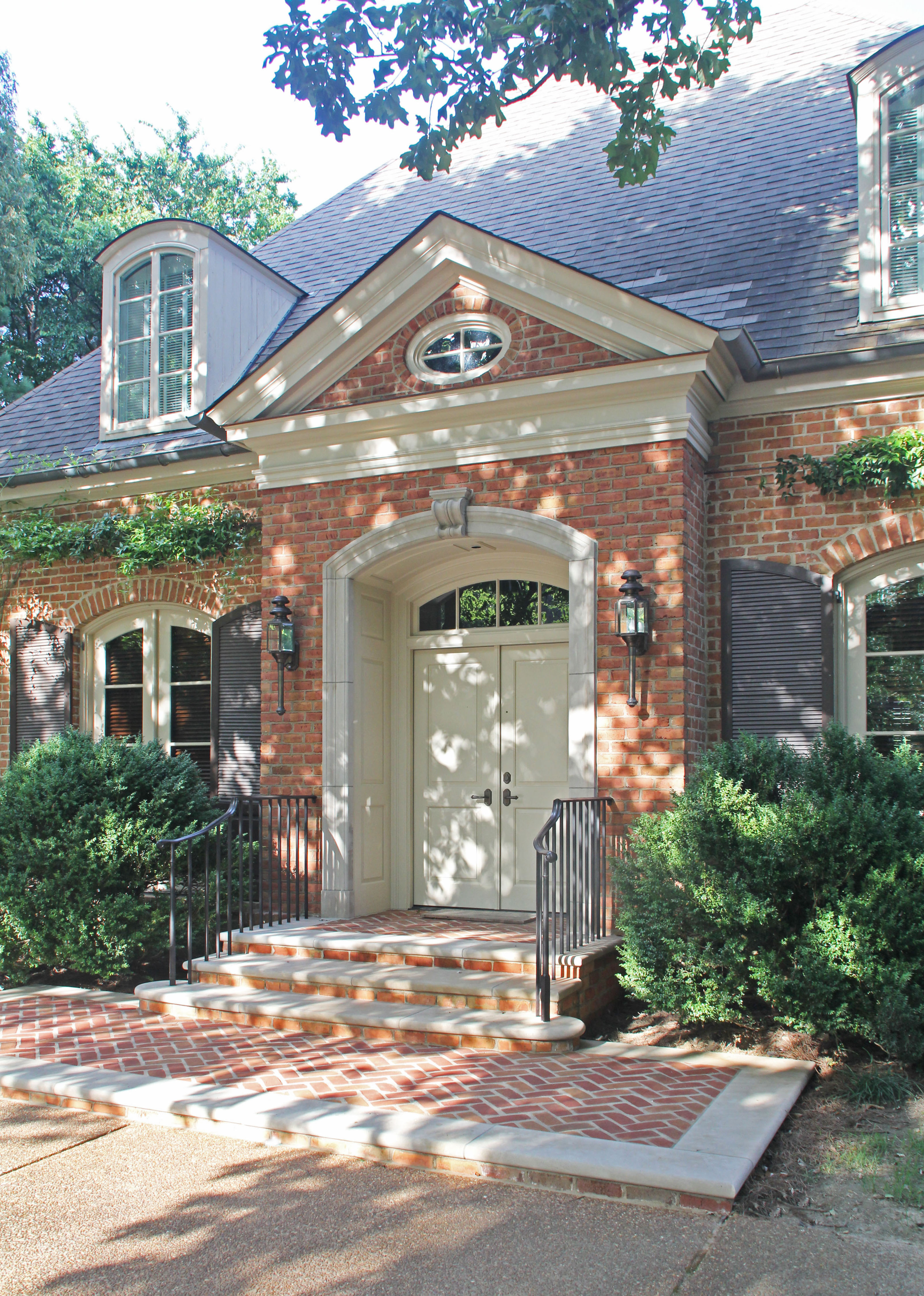 Red brick house with matching driveway, featuring a large white front door.