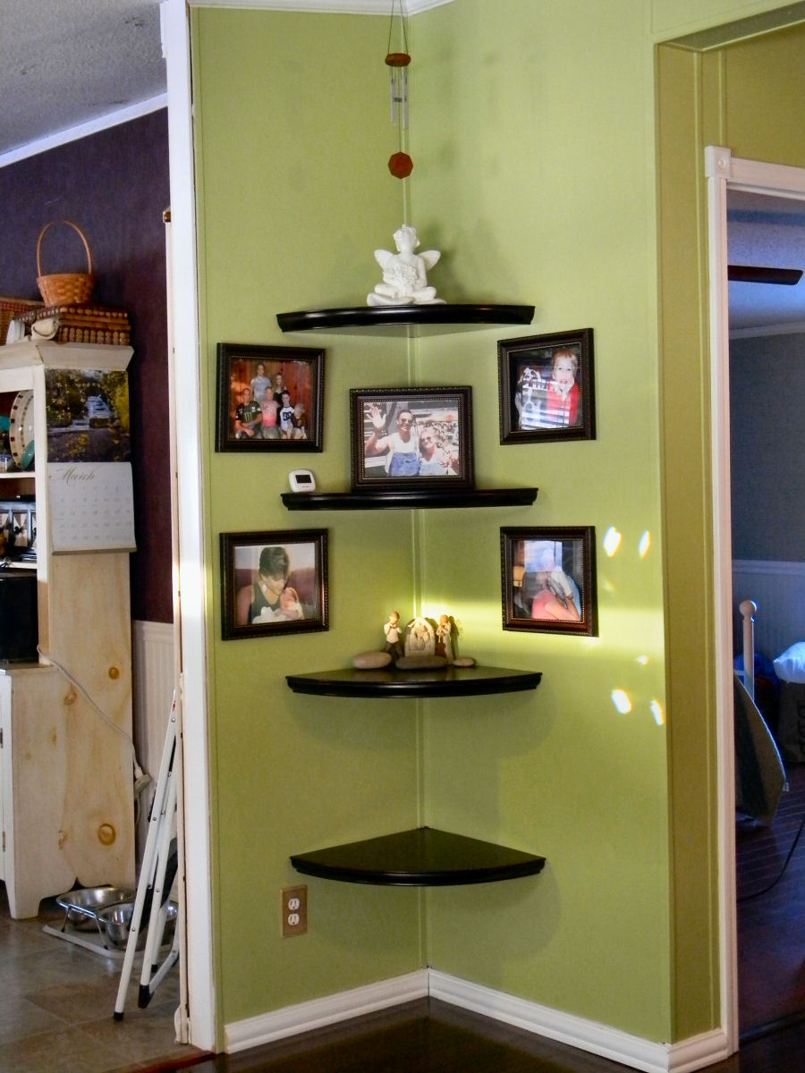 Green wall with corner-mounted floating shelves holding pictures, stones, and small sculptures.