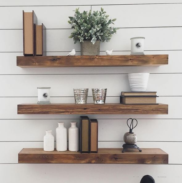 Three floating shelves, holding a plant, books, and small buckets.