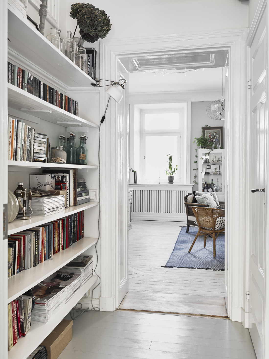 A white hallway with a bookshelf flanked by another room that has a chair.