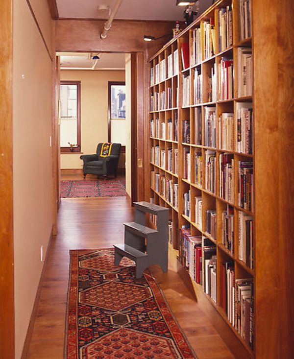 Hallway with a wooden bookshelf lining the wall with a red carpet on the floor.