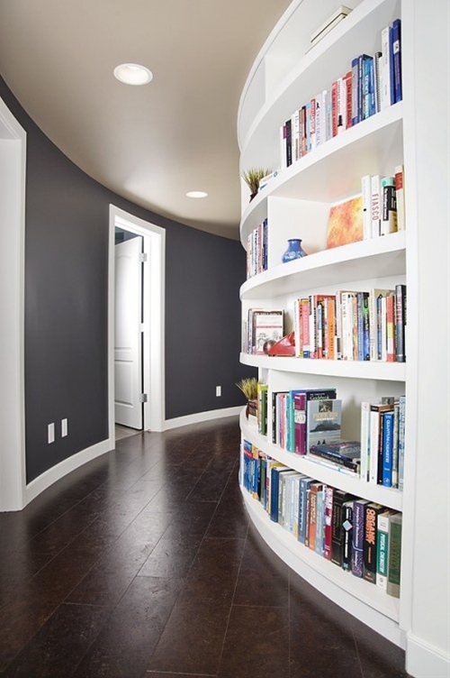 A hallway with a curved wall showcasing a bookshelf filled with various books and decorative items.