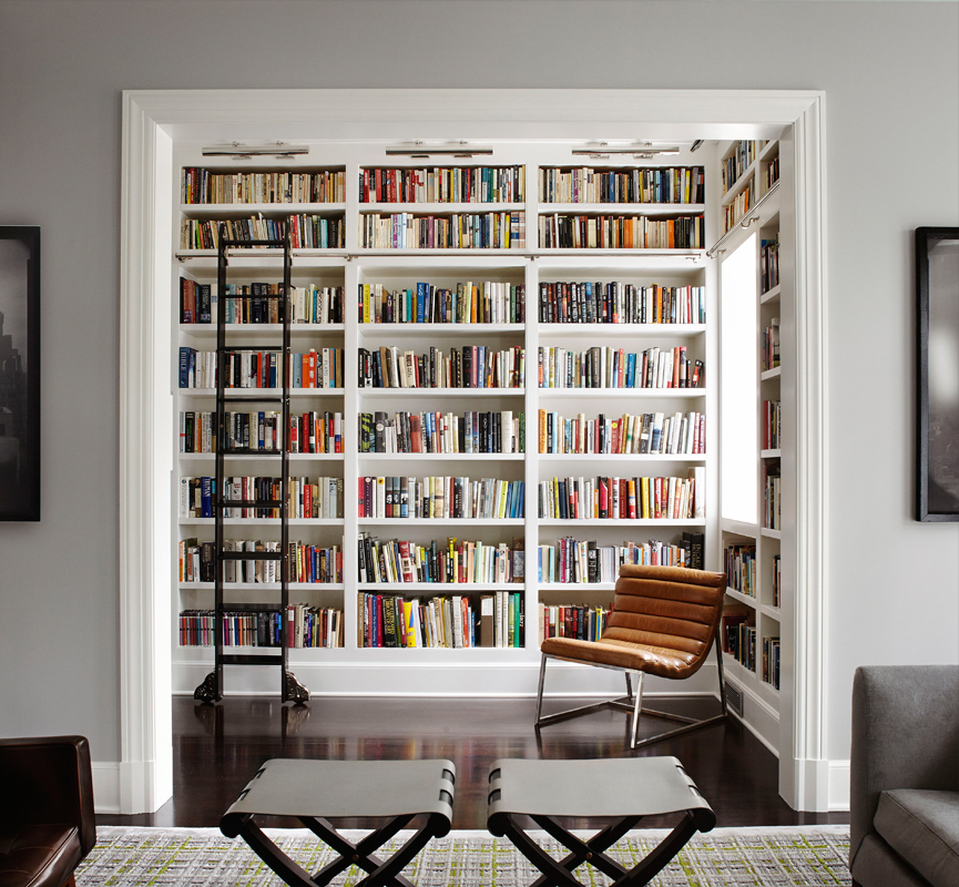 A spacious living room featuring a sizable bookcase filled with books, featuring a ladder.