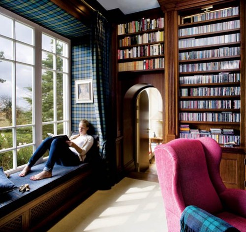 A woman sitting in a chair by a window surrounded by bookshelves.