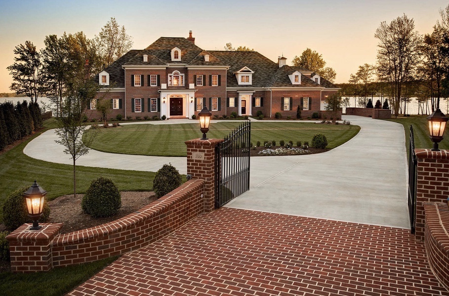 Massive driveway with metal fence gates leading up to a mansion made of red brick.