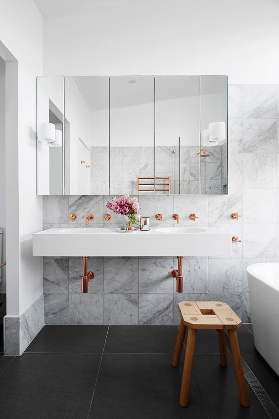 A luxurious bathroom featuring marble walls and black flooring accented by hints of copper fixtures.