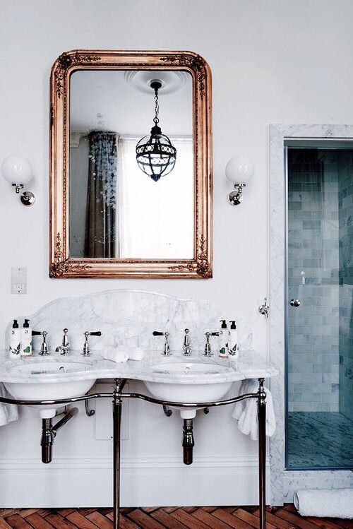 Marble double vanity flanked by a mirror with a copper frame.