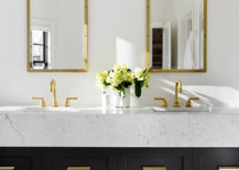 White bathroom with black drawers, finished with gold fixtures.