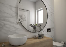 A contemporary bathroom featuring sleek white marble walls, adorned with a circular mirror and wood vanity.