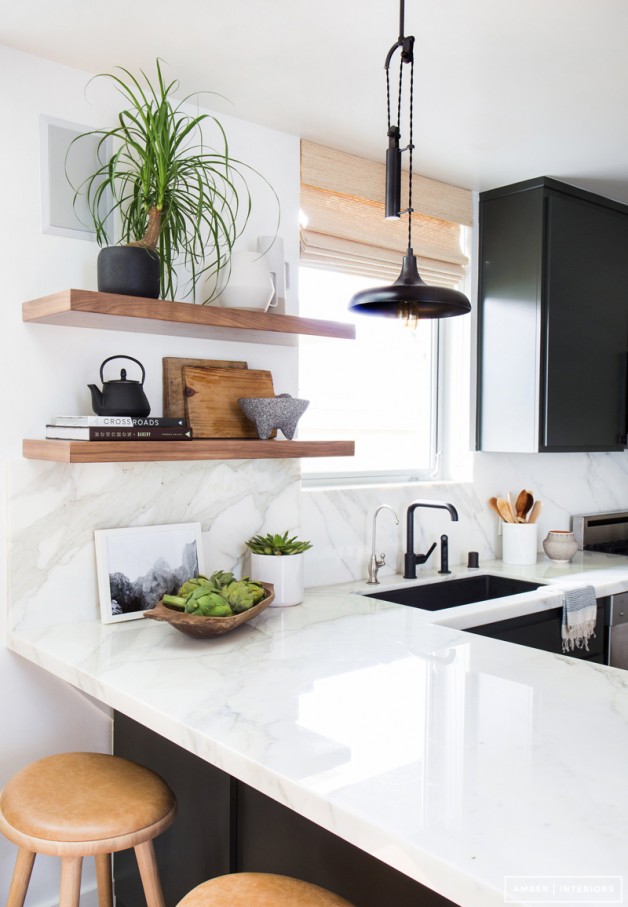 Minimalist kitchen with L-shaped countertop and wooden floating shelves.