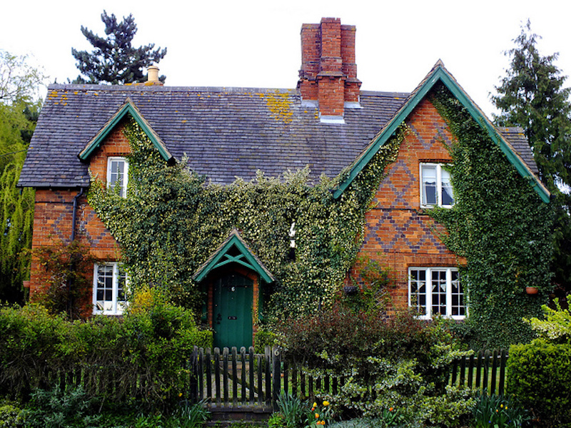 red brick house with ivy growing on the walls and features green trim.