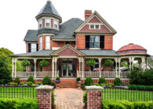 Large red brick house with entryway, black fencing, and white deck pillars.