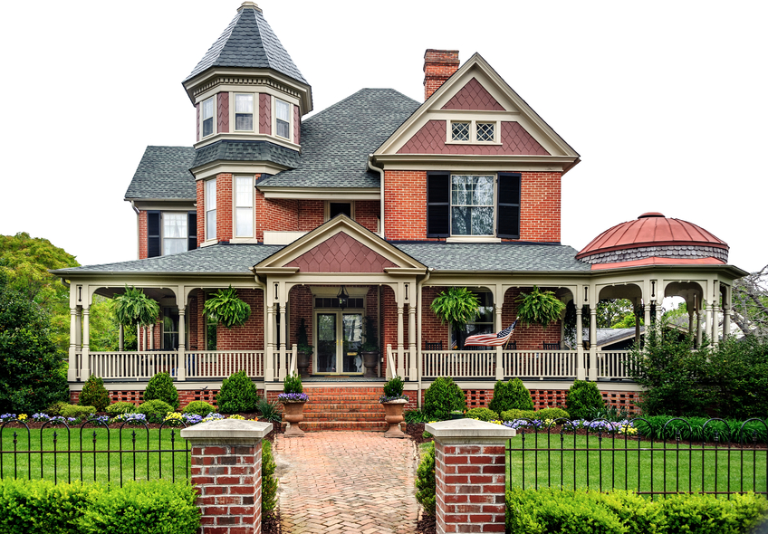 Large red brick mansion with entryway, black fencing, and white deck pillars.
