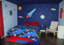 Bed on top of foam squares flanked by space wall art the includes a rocket, UFO, Earth, and the sun.