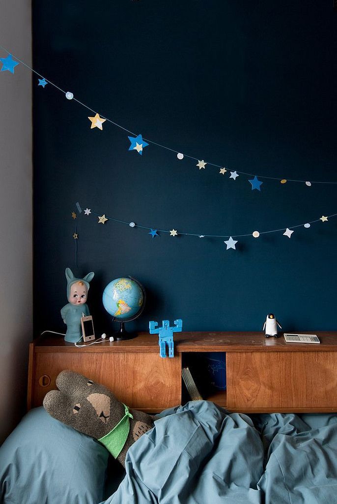 Zona de quarto infantil com peluche aninhado no edredão, ladeado por recortes de estrelas pendurados num barbante.