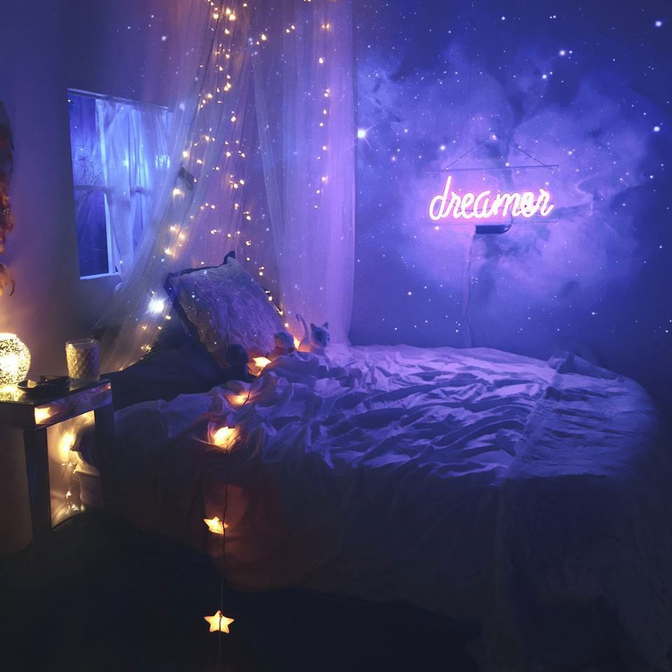 Quarto infantil espacial com luzes amarelas com tema de estrelas e um letreiro de néon roxo brilhante que diz "sonhador."