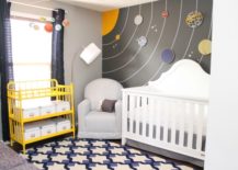 Space nursery with solar system wallpaper, white crib, and a yellow changing table.