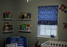 Space nursery with lights on the ceiling, a white crib, and a blue chair flanked by floating shelves.