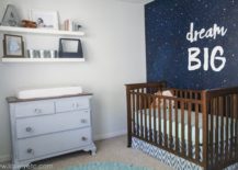Space nursery with a dark wood crib and a star-themed wallpaper with the words "dream BIG."