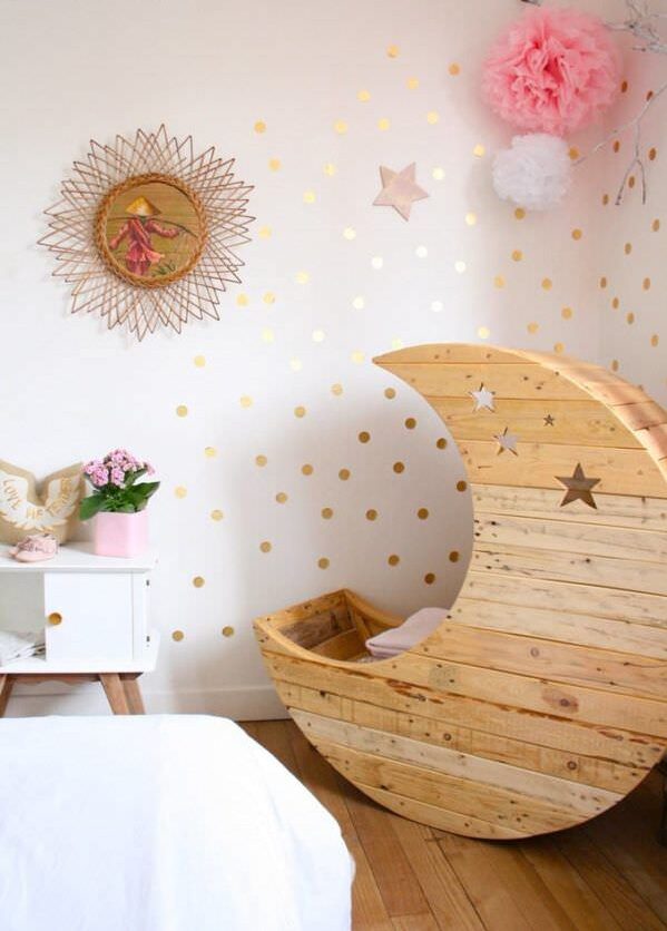 Berçário com tema espacial e cama em forma de lua crescente ladeada por decorações de parede.