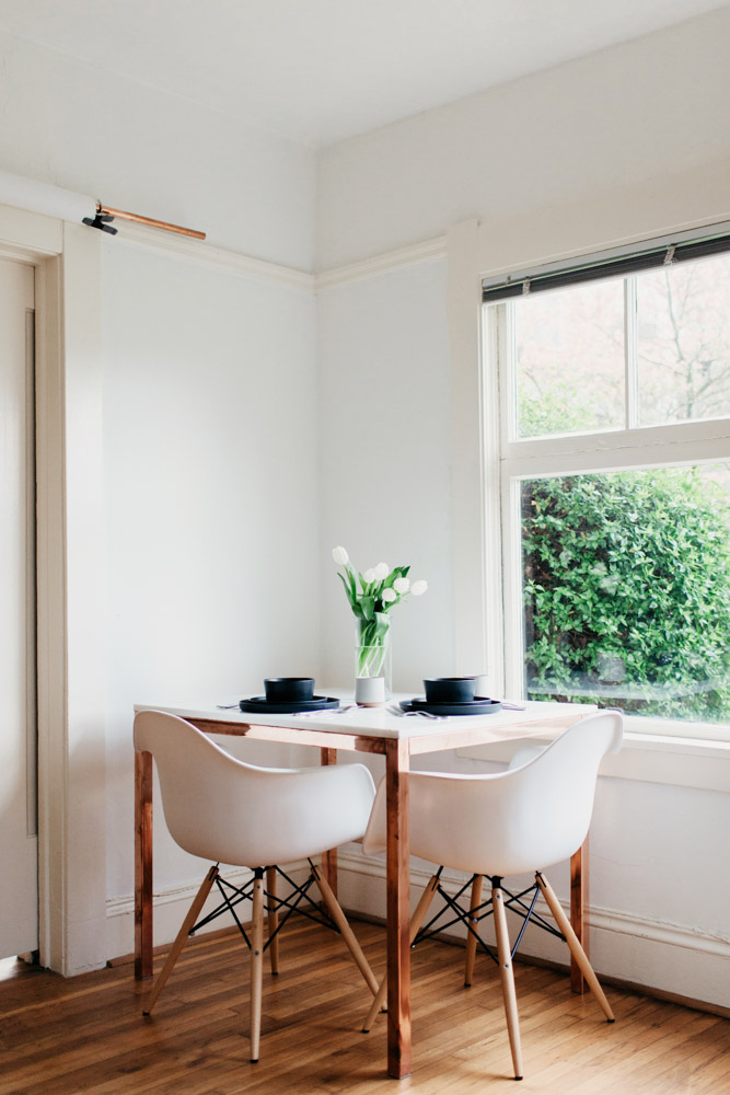 A room with a white table and chairs. The table is neatly set with chairs placed around it. The room is well-lit, creating a bright and inviting atmosphere.