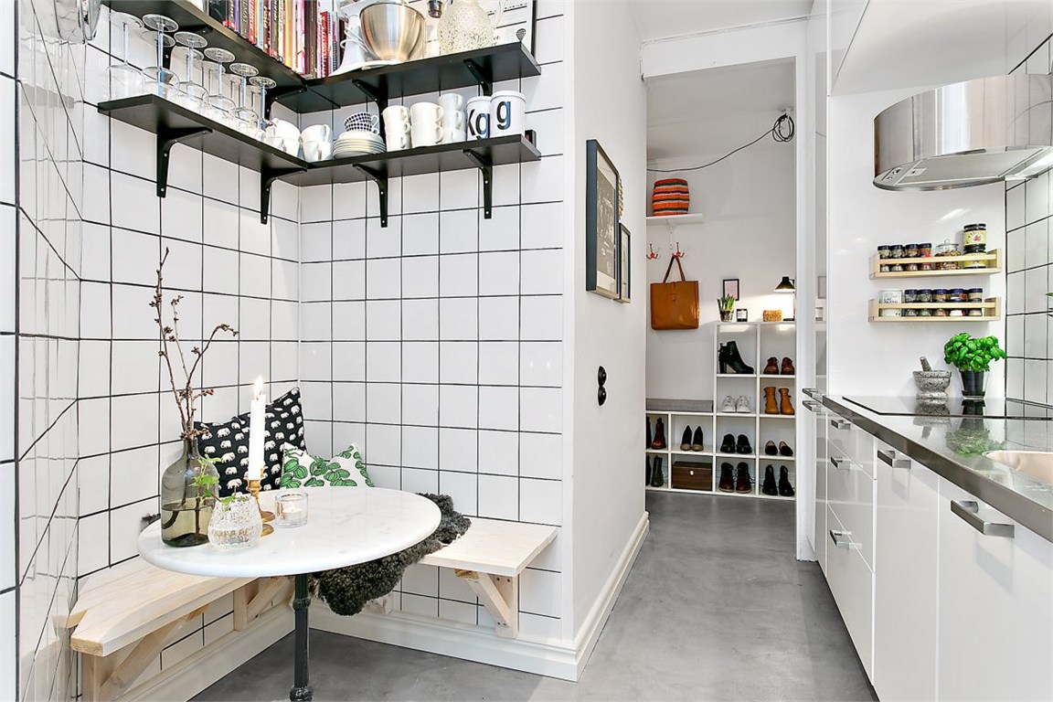 A small kitchen with white tile walls and shelves. Wall-mounted bench seats with a round table.