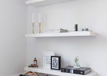 Four white floating shelves with picture frames, candles, and books.