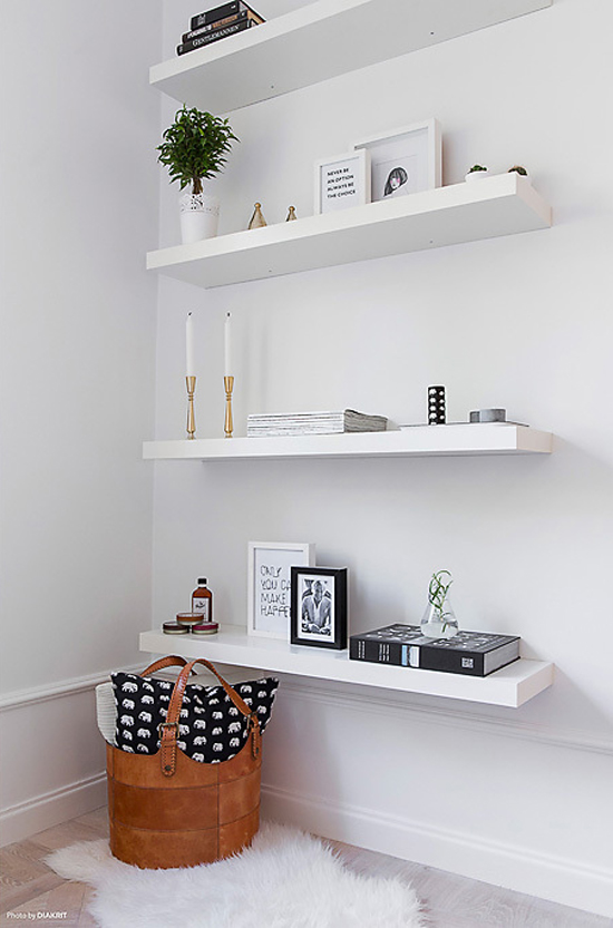 Four white floating shelves with picture frames, candles, and books.