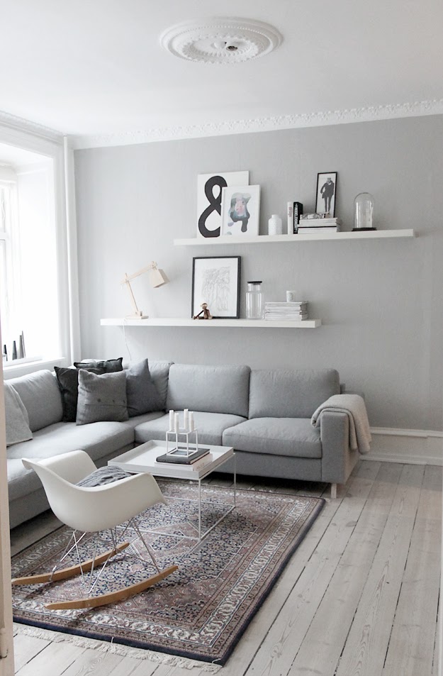 Modern living room with two white floating shelves featuring a lamp, pictures, and glass containers.