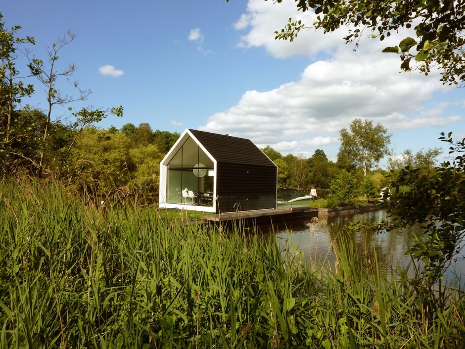 Tiny home with black exterior and white edges near a body of water.