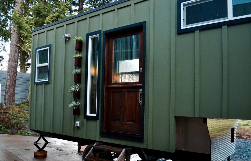 Elegant green exterior of a tiny home, featuring a wood front door and a slit window.
