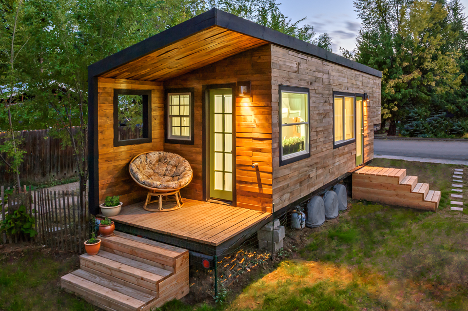 Rustic tiny home exterior finished in wood and has a cozy circular outdoor seat.