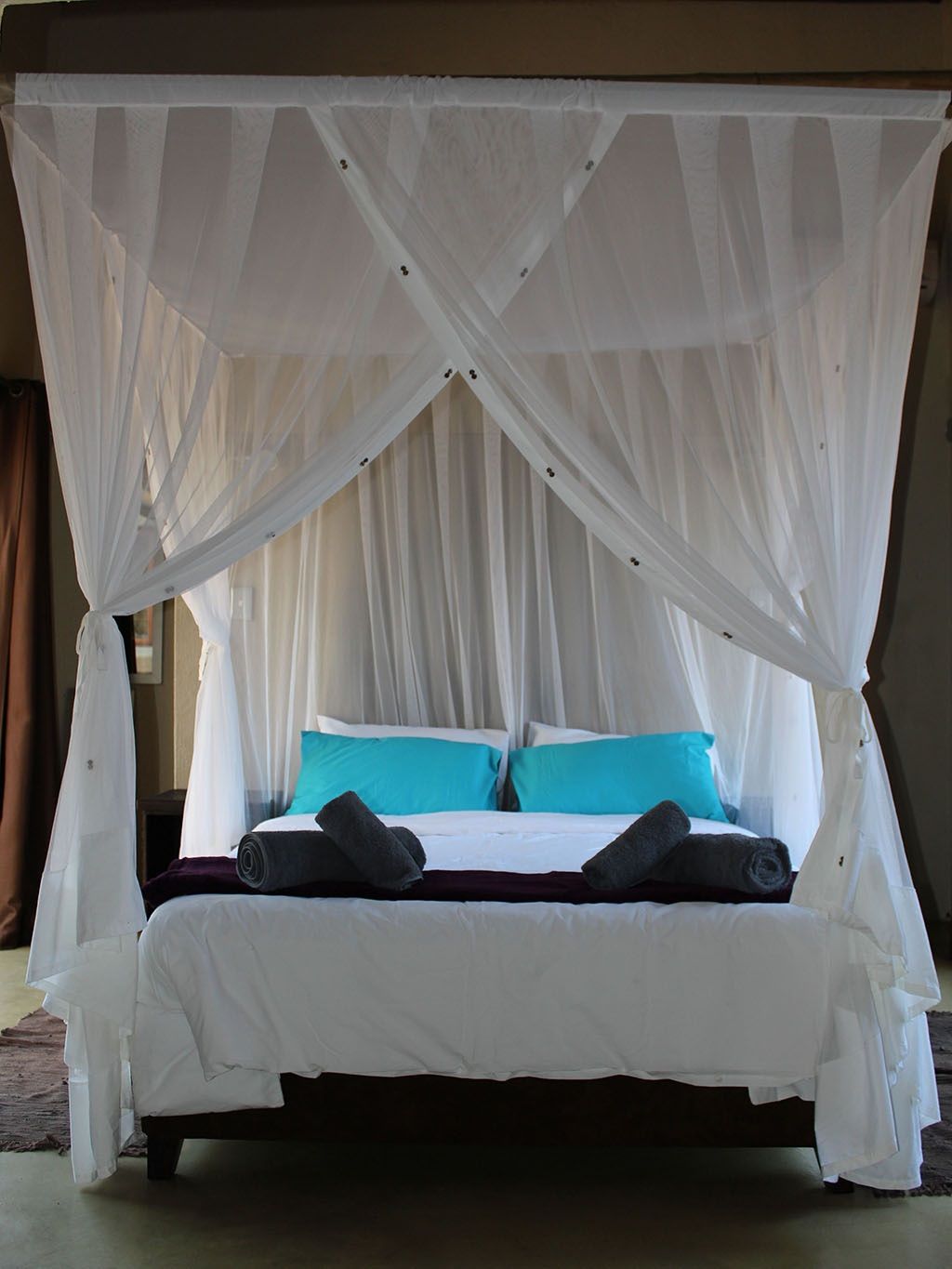 Four poster bed with white canopy curtains and turquoise pillows
