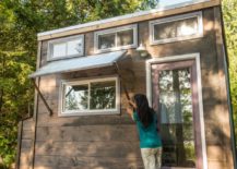 Person adjusting window shade on the exterior of a tiny home that has multiple windows and wood exterior finish.