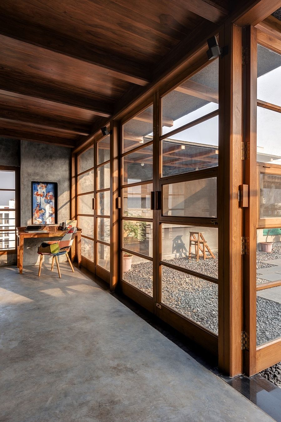Glass windows and doors with wooden frame connect the interior with the patio