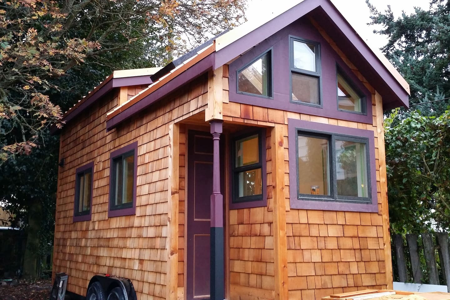 Wooden exterior of a tiny home accented by purple, featuring sizable windows with green frames.