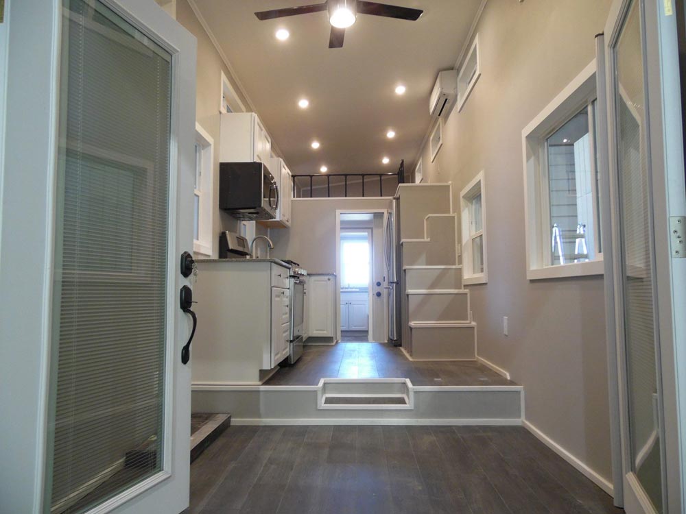 Interior of a modern tiny home with wood floor and white accents, with the focal point being unique stairs.