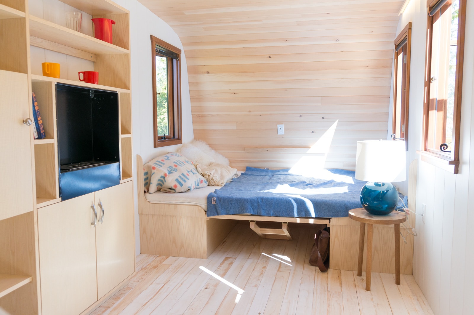 Interior of a tiny home that has wood on the floors and ceiling, matching the white walls and wood furniture.