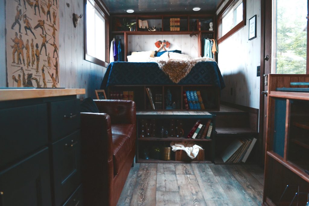 Old fashioned interior of a tiny home, featuring a green finishes, leather couch, and a rack of books.