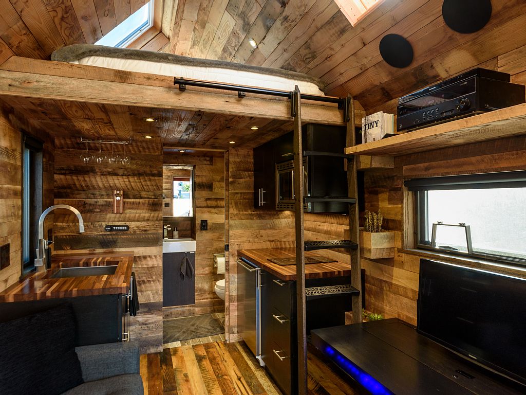 Interior of tiny home with modern technology embedded within the wood-centric finishes of almost all furniture.