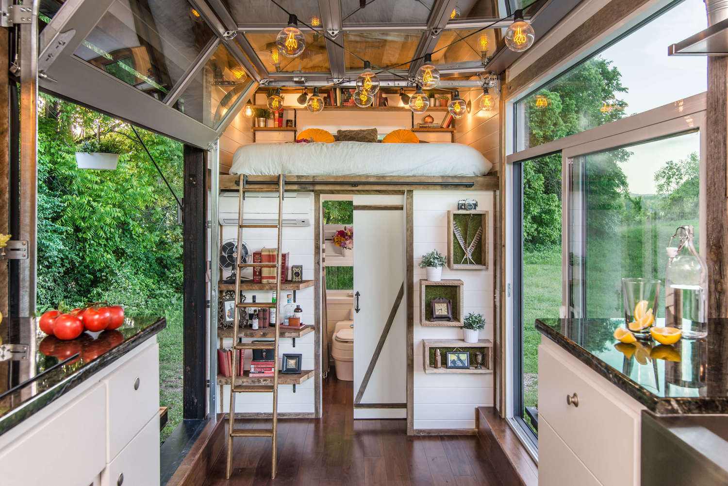 Interior of tiny home with multi-level living space, showcasing a ladder to the bed and white/wood finishes throughout the design.