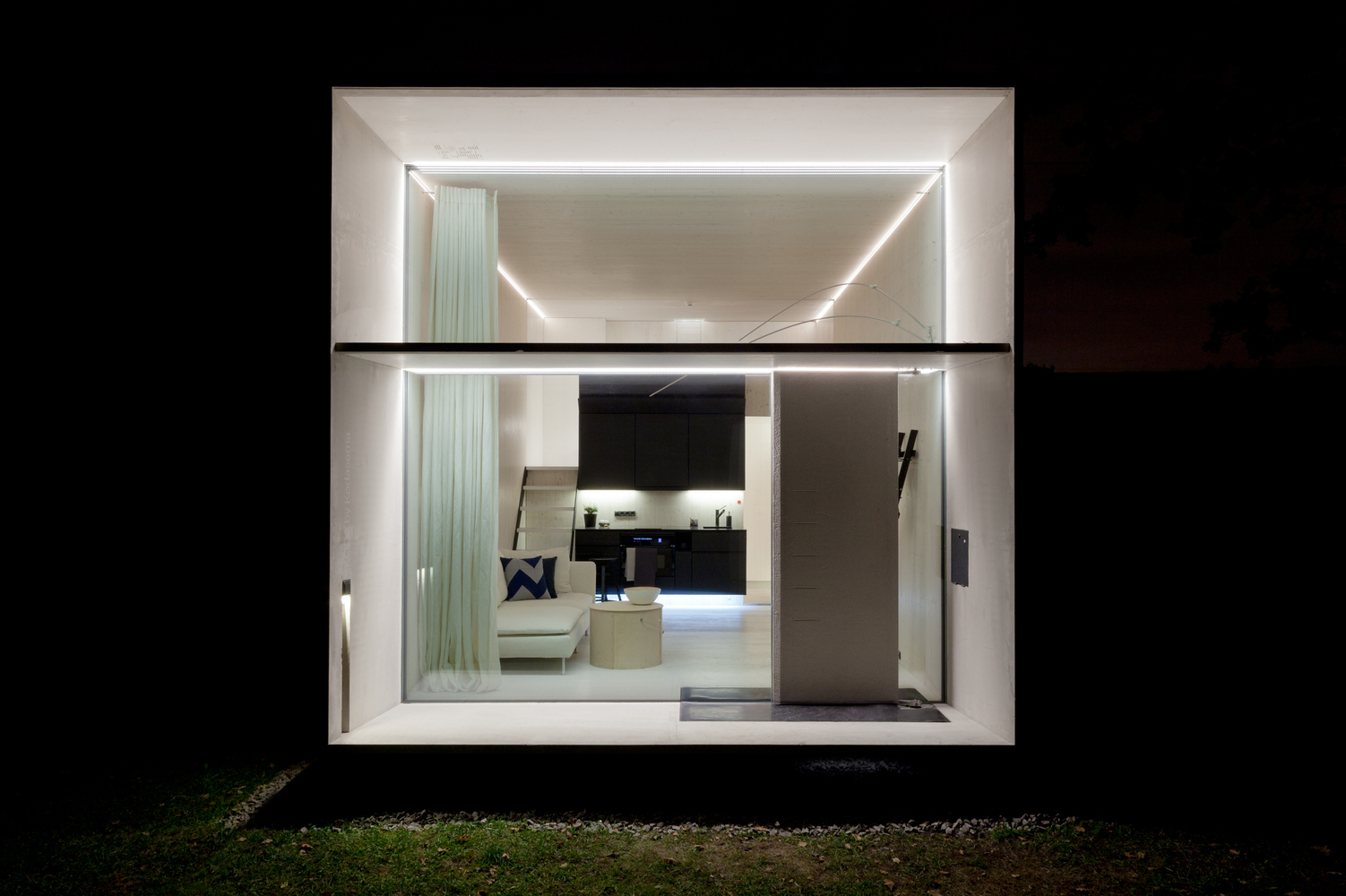 A night-time picture of a tiny home with front glass lit up to show the modern interior.