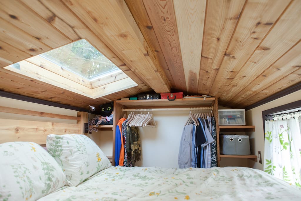 Interior of tiny home with wood ceiling, skylight, flower-themed bed covers, and a closet for clothes.