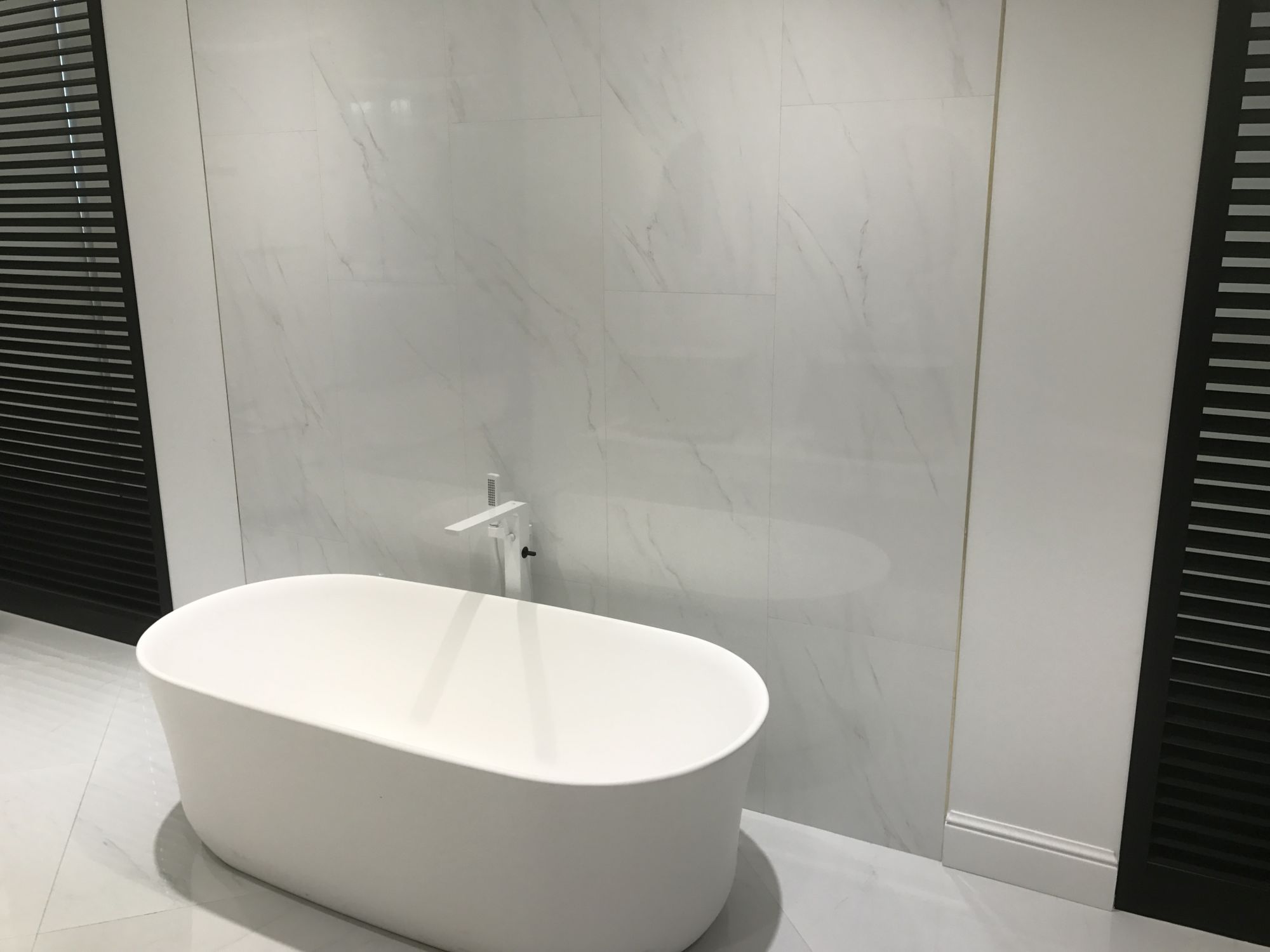 Marble looking wall tiles with white shaped round bath tub by Porcelanosa