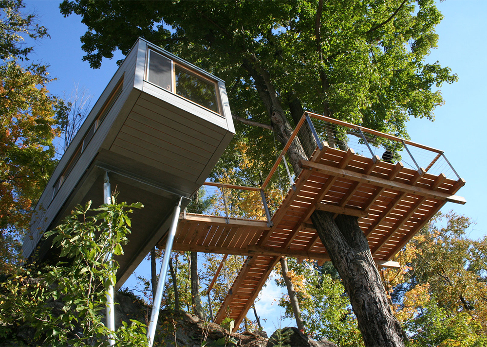 A modern treehouse with a deck in a shade of a tree